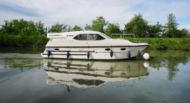 Side view of the Countess on a quiet canal, its sleek profile reflected in the still water beneath a bright blue sky.