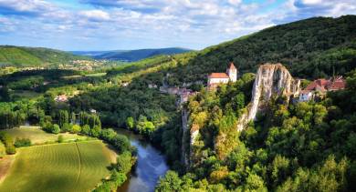 Scenic view of the Lot River at the base of tall limestone cliffs with lush greenery on both sides.