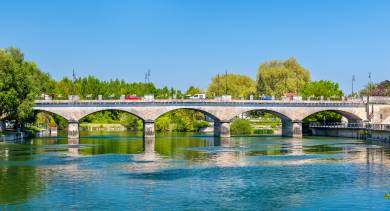 View of Pont Neuf in Cognac crossing the Charente River, with cars and pedestrians passing over the calm water.