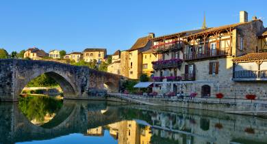 Café terraces overlooking the river beside a historic bridge in Aquitaine.