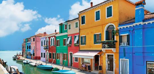 Una fila di case dai colori vivaci si riflette in un canale tranquillo sull’isola di Burano, nella regione Veneto.