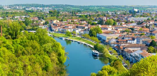 Vue aérienne d’Angoulême avec des bateaux sur la Charente et des berges arborées longeant le quai.