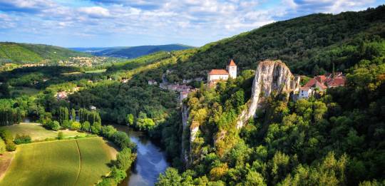 Vue pittoresque de la rivière Lot au pied de hautes falaises calcaires, entourée de verdure luxuriante.