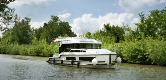 Liberty boat gliding gently on the water, with lush foliage along the banks and soft summer skies above.