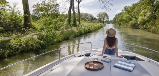 Ruhiger Moment allein – eine Frau blickt vom Bug aus auf den baumgesäumten Fluss.