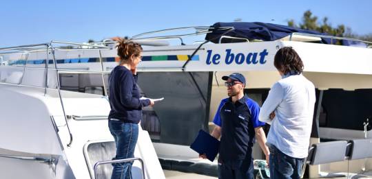 A Le Boat team member chats with customers on the quay in front of moored boats.