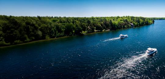 Two Horizon boats cruising side by side along a green shoreline on the Rideau Canal in Ontario under a clear sky