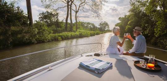 Romantic sunset moment for a couple enjoying drinks at the front of their boat on a peaceful canal.