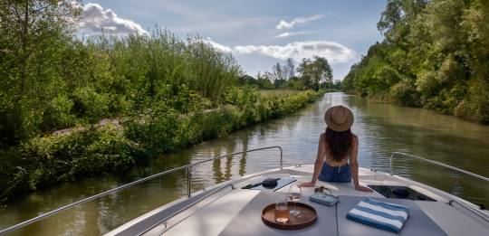 Tranquil view from the boat as a woman lounges under blue skies on a scenic river cruise.