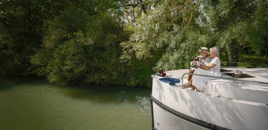 Un couple observe les oiseaux depuis l'avant de leur bateau, entouré d'une végétation luxuriante.