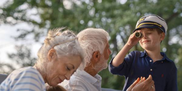 A child looks through a monocular on the boat deck while cruising, enjoying a fun family adventure on the water with grandparents and a sister.