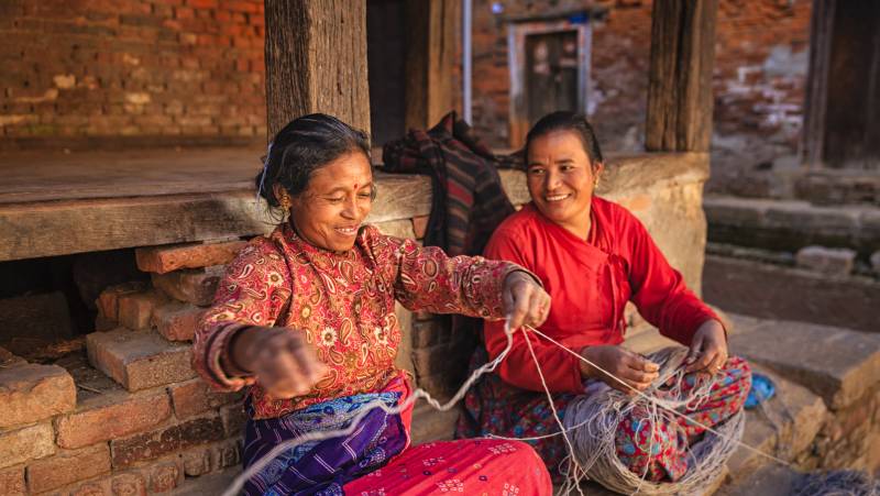 Nepali women spinning a wool in front of the house.