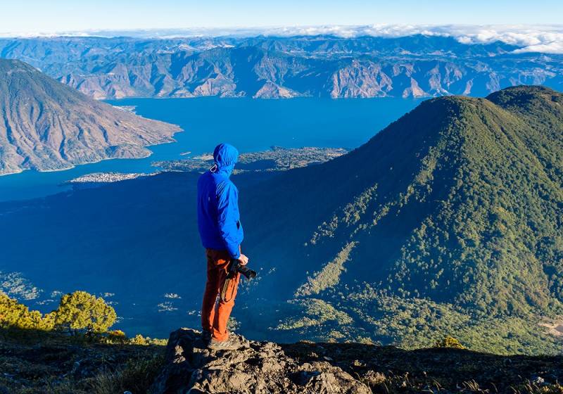 Guatemala travel guide - Enchanting TravelHiker with panorama view of Lake Atitlan and volcano San Pedro and Toliman early in the morning from peak of volcano Atitlan, Guatemala. Hiking and climbing on Vulcano Atitlan
