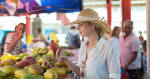 Female traveler wearing elegant colonial style white tunic and hat buying fresh tropical fruit on traditional Victoria food market on Seychelles islands