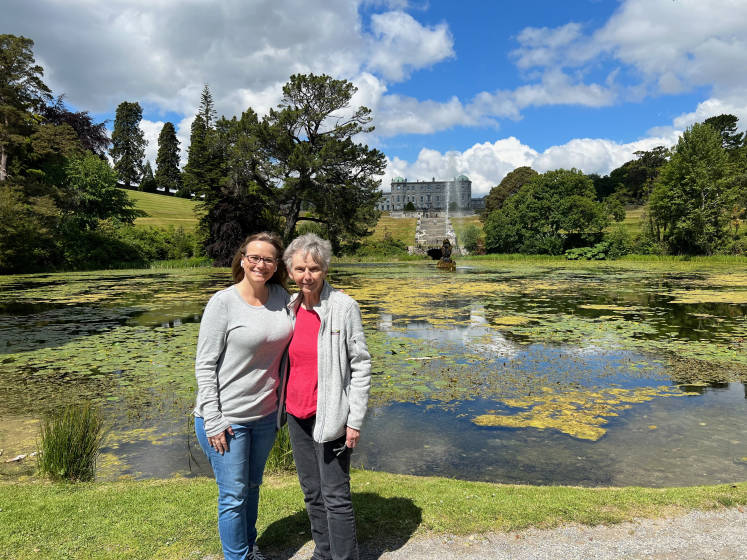 two womwn standing in front of a waterbody with a castle in the backdrop
