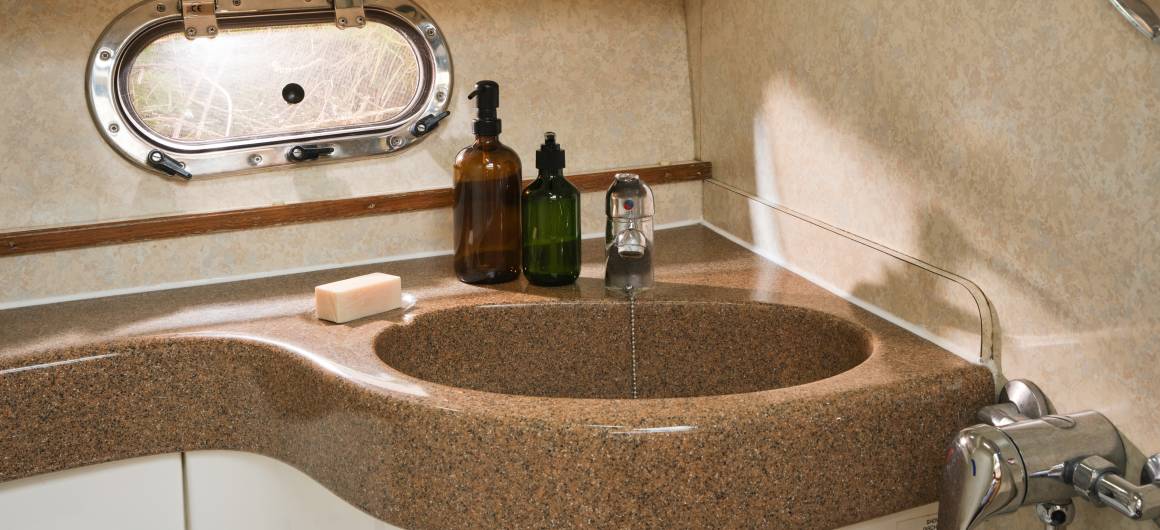Modern bathroom in the Consul with a curved brown sink, soap dispensers, and a small porthole window for natural light.