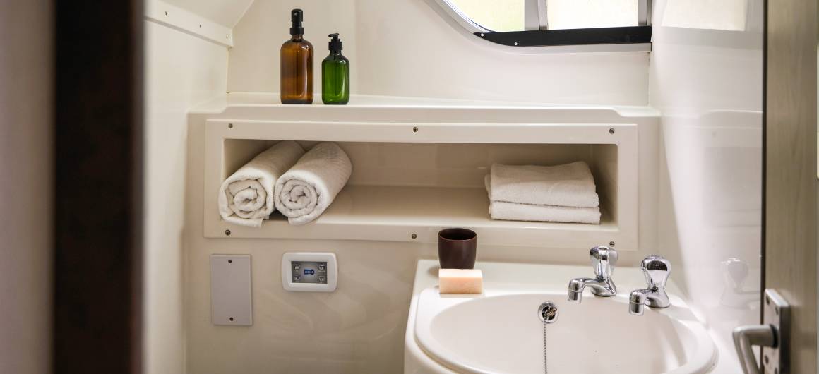 Compact bathroom aboard the Continentale with a rounded white sink, chrome taps, shelf with towels, and elegant soap dispensers beside a window.