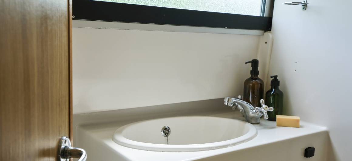 Bathroom interior of the Dancer 4 with a round sink, classic taps, and toiletries by the window.