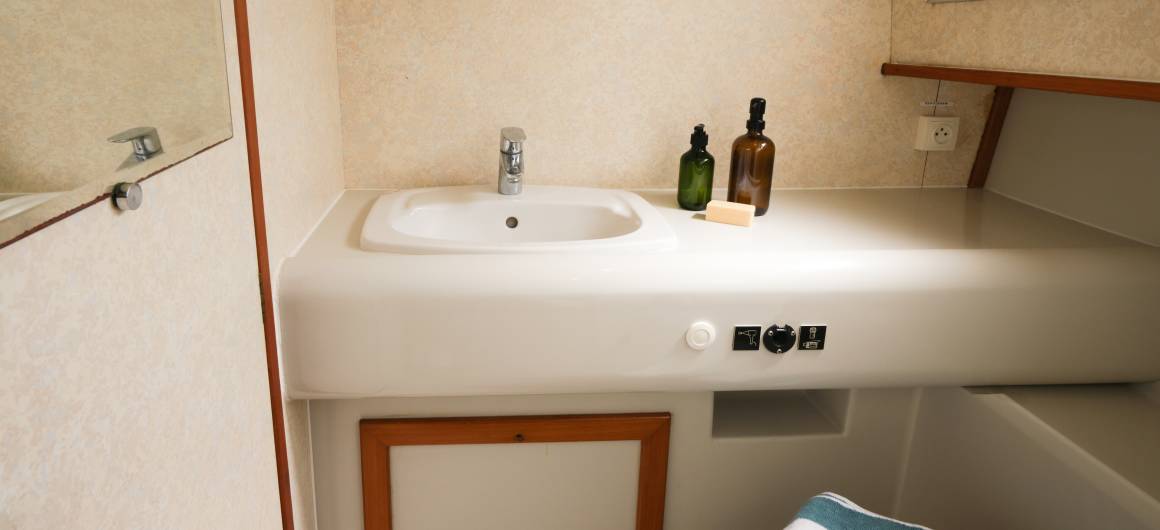 Clean and spacious bathroom aboard the Grand Classique, with a wide white basin, soap bottles, and a mirror reflecting the soft interior light.