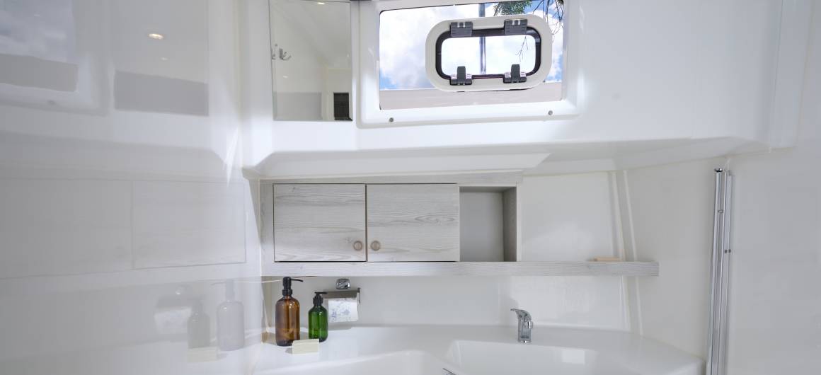 Crisp white bathroom aboard the Horizon 5 with a wide basin, toiletries, overhead cabinets and a window bringing in daylight.