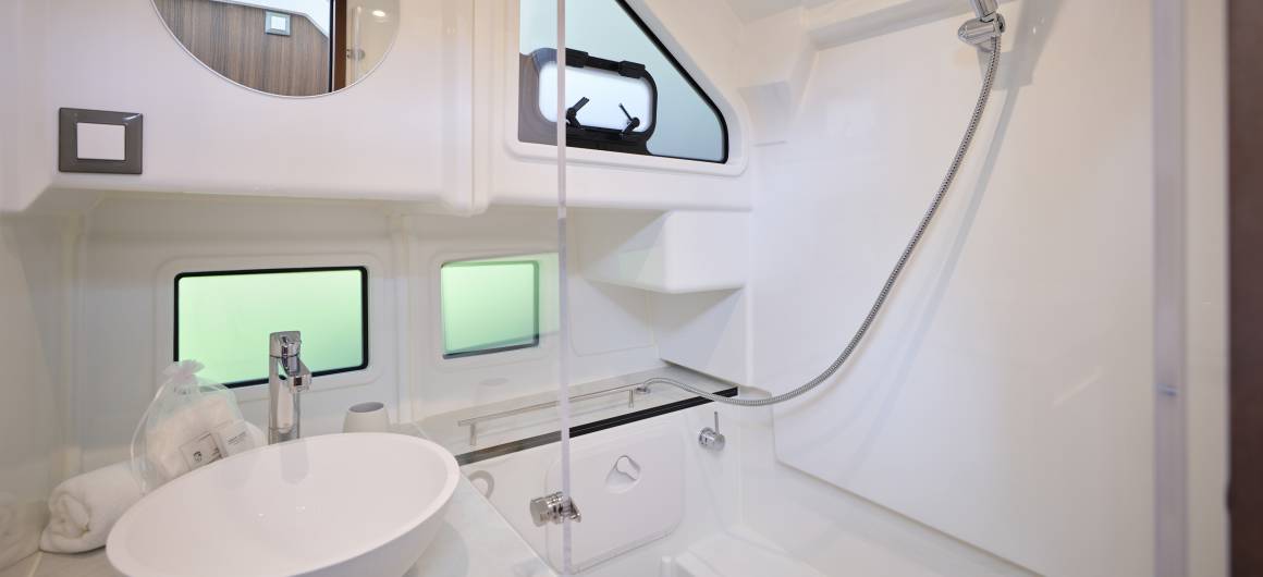 Modern bathroom aboard the Liberty featuring a rounded sink, glass shower screen, and clean white finishes with natural light streaming in.