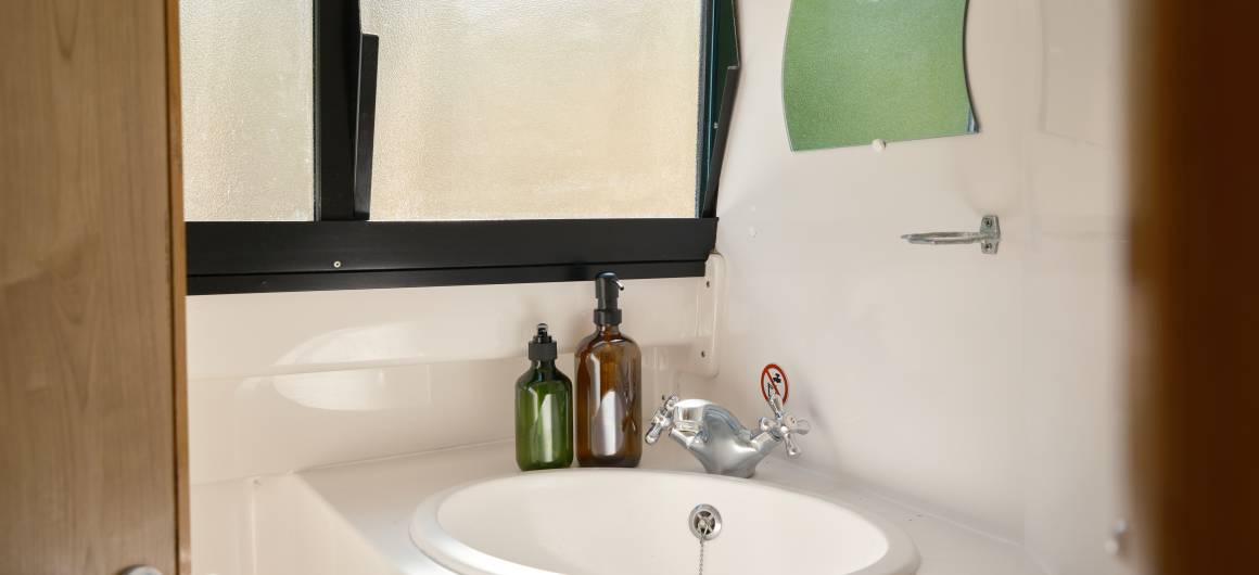 Functional bathroom aboard the Magnifique, with a rounded basin, glass bottles, and soft daylight shining through frosted windows.