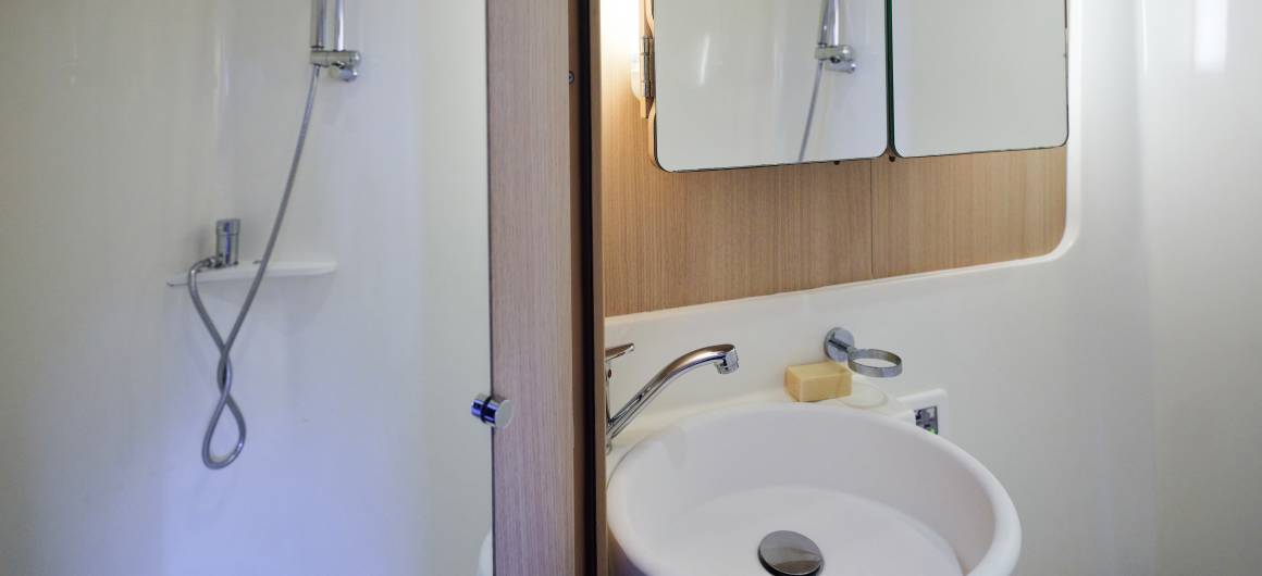 Compact bathroom with sink, mirror and shower inside the Vision 4 boat.
