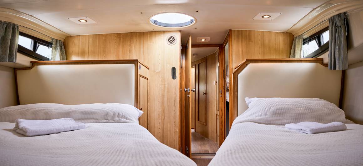 Larger twin bedroom on the Elegance boat, with plush bedding, wood interiors, and a central skylight casting soft light over the space.