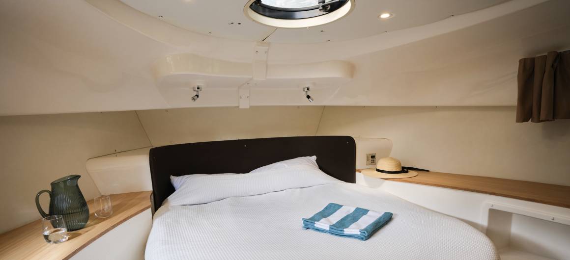 Front cabin featuring a double bed with striped towels and a windows for natural light.