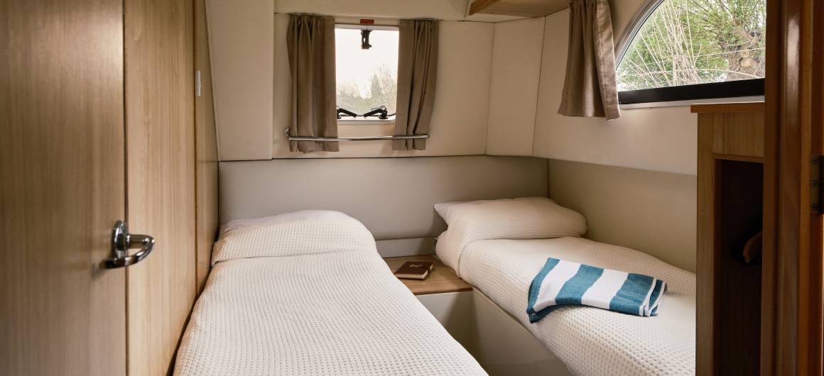 Compact twin cabin aboard the Dancer 3, with two neatly made single beds, warm wooden tones, and soft daylight filtering through curtained windows.