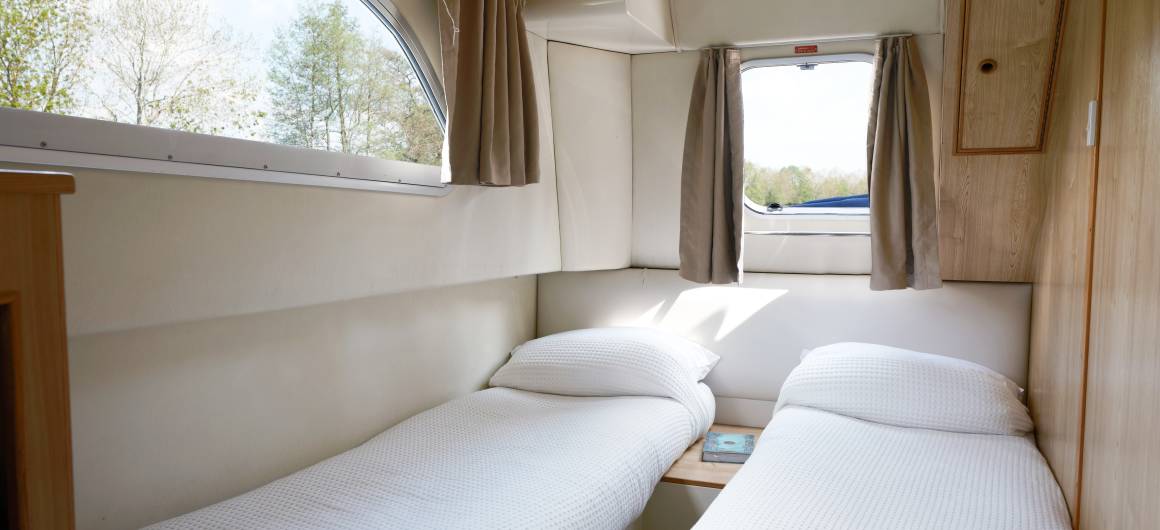 Bright twin cabin aboard the Magnifique, with two single beds placed beneath large windows that let in views of the surrounding trees and sky.