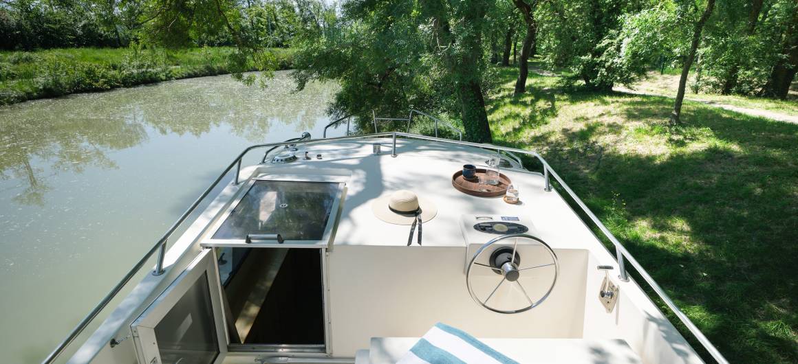 Top deck of the Countess with a shaded helm and lounging area, moored peacefully by the riverside.