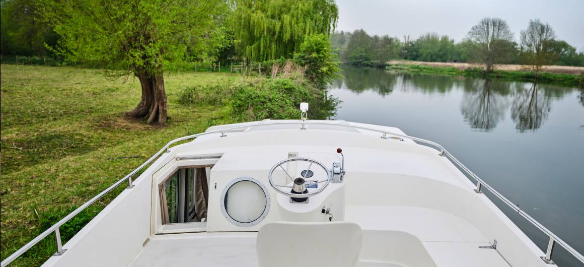 Top deck of the Continentale with white helm station overlooking a peaceful riverbank lined with trees and reflected greenery.
