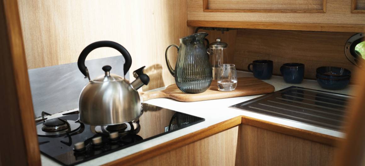 Kitchen inside the Countess featuring a kettle on the stove, glassware, and a wood-trimmed counter.