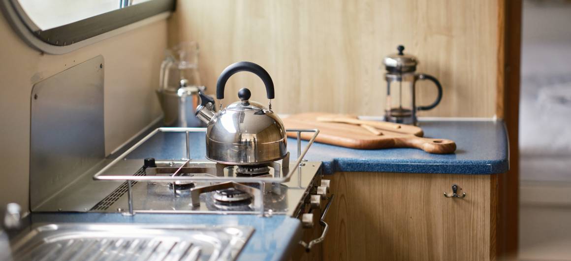 Functional kitchen space aboard the Dancer 3 with a silver kettle on the hob, blue countertop, and wooden cutting board beside a French press.