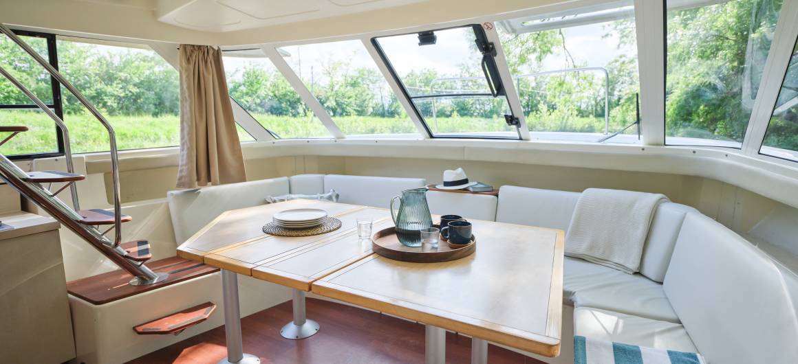 Spacious saloon area with large windows, modern table setting and cosy white seating aboard the Vision 4.