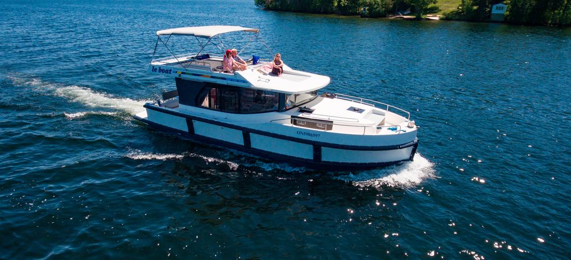 Aerial view of a lone Horizon boat cruising on the Rideau Canal, surrounded by vast water and low wooded islands.
