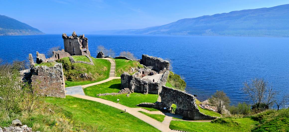 Ruinen einer mittelalterlichen Burg auf einer Klippe mit Blick auf das tiefblaue Wasser des Loch Ness in den schottischen Highlands.