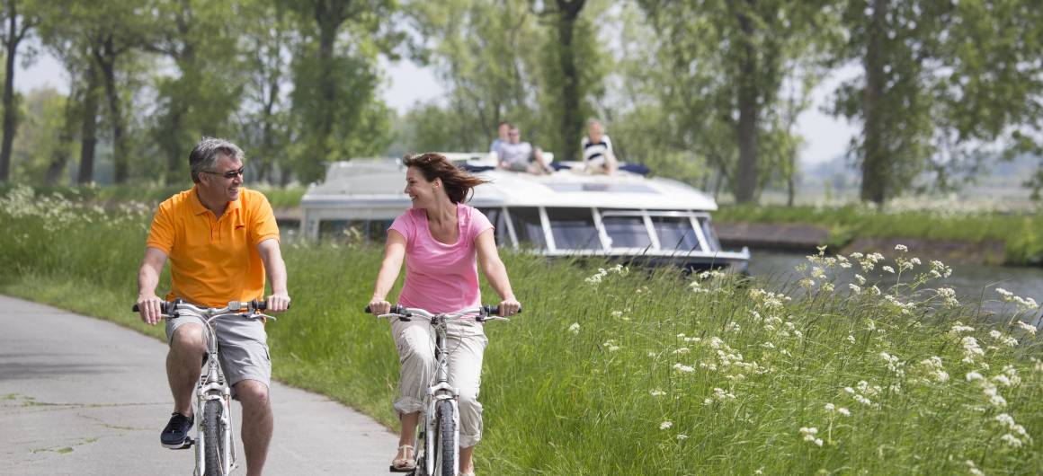 Cyclist riding along a peaceful canal beside a moored boat, active holidays in the Belgian countryside.