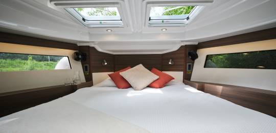Bright front cabin aboard the Liberty with a wide bed, skylights above, and panoramic windows bringing in lush riverside views.