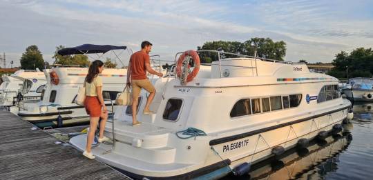 Two people boarding a Le Boat cruiser from the marina pontoon on a calm evening.