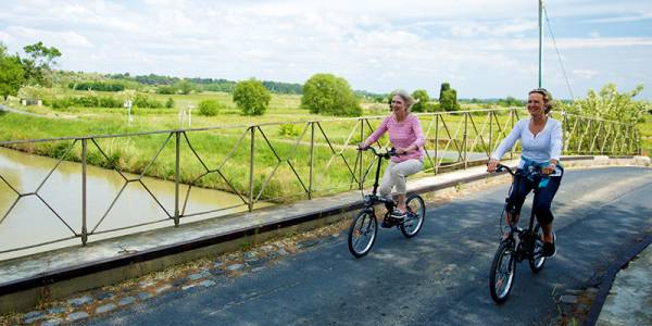 Two women cycling across the bridge on the Canal du Midi