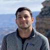 Ben Burtis smiling outdoors in a gray Patagonia fleece, with rocky canyon landscape in the background.