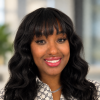 Bre Epps smiling, with long wavy black hair with bangs, nose ring, silver necklace, and patterned white blouse.