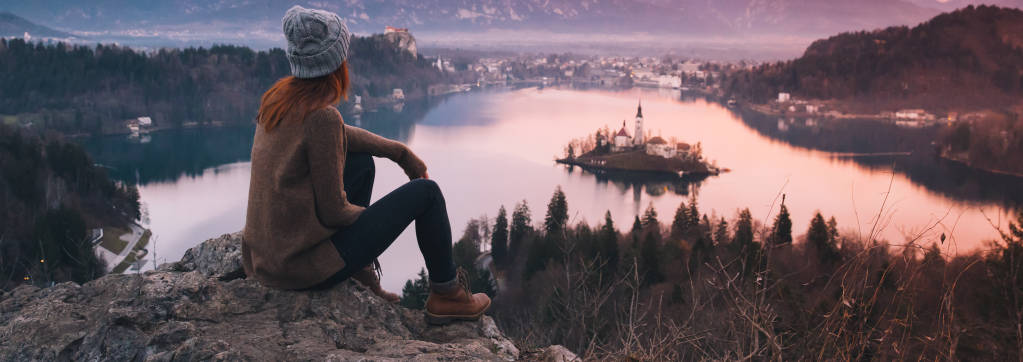 Woman looking on Bled Lake with Island, Castle and Alps Mountain on background.