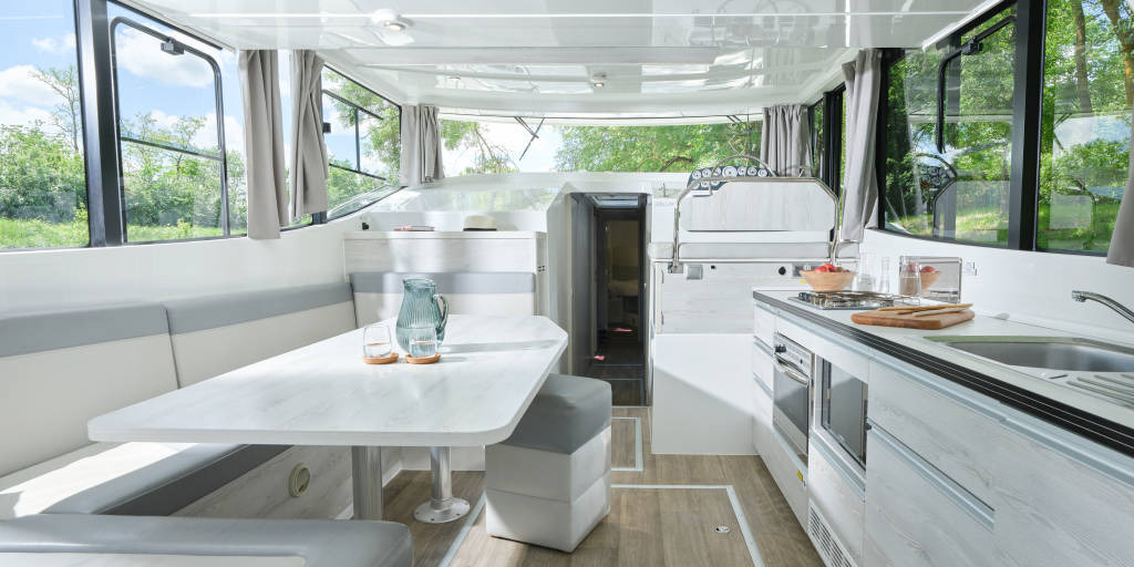 Bright and modern saloon aboard the Horizon 5 with wraparound windows, a white dining table, compact kitchen, and neutral tones throughout.