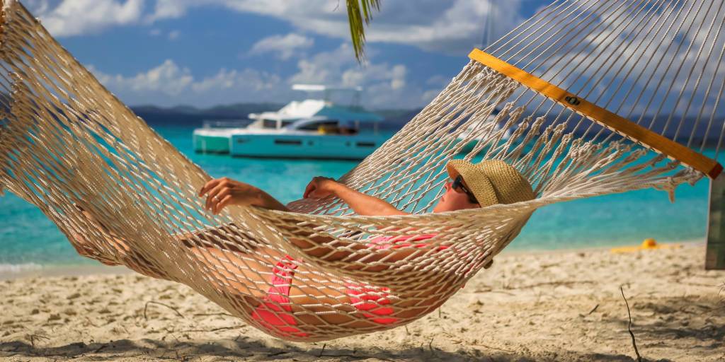 Woman relaxing in hammock with power catamaran in the background