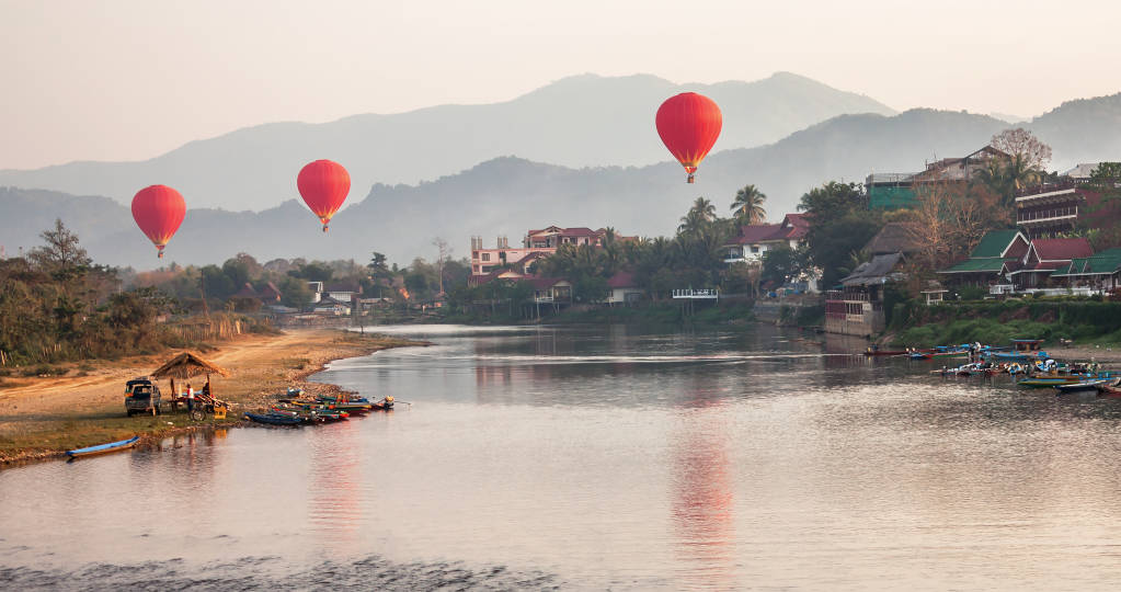 Concept recreation: hot air balloons flying over the river Nam Song at sunrise. Vang Vieng, Laos, Asia