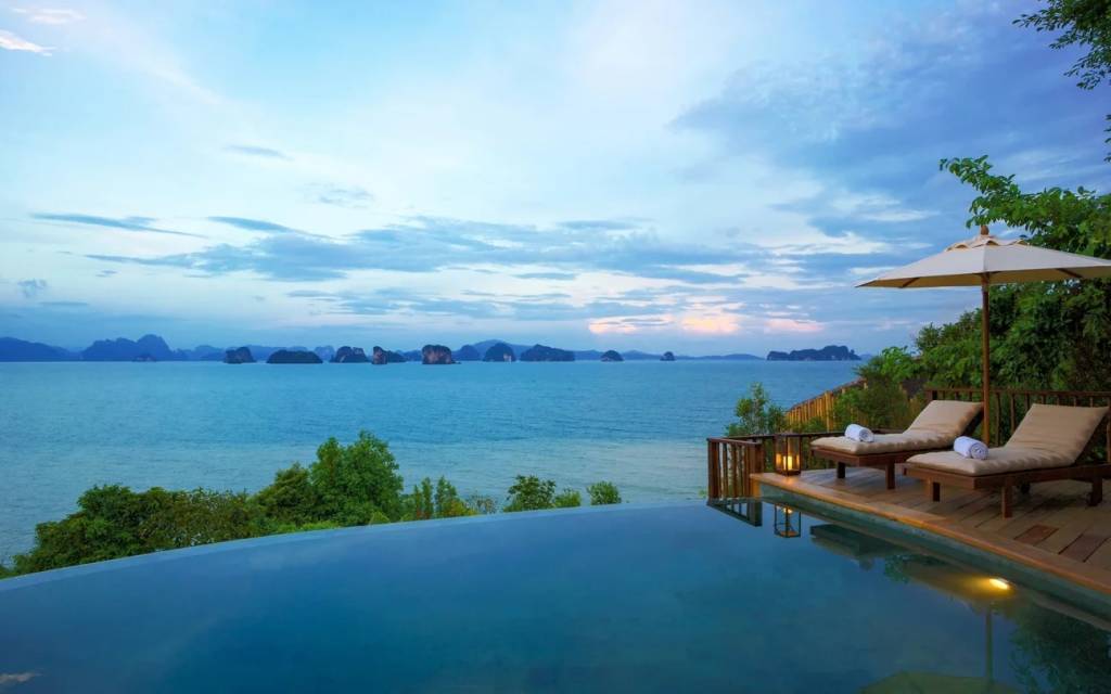 Privater Infinity-Pool mit zwei Sonnenliegen in der Abenddämmerung, mit Blick auf die Bucht von Phang Nga