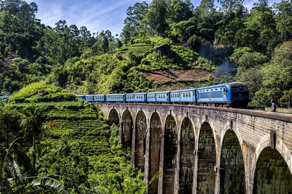 Ein blauer Zug überquert die Nine Arches Viaduktbrücke im grünen Hochland von Sri Lanka